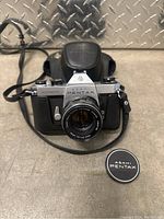 Front view of Asahi Pentax Spotmatic camera with lens and lens cap on surface.