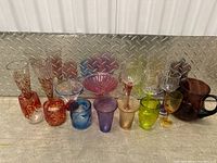 Front view of assorted colored glassware including tumblers, vases, and stemmed glasses in red, blue, pink, purple, green, amber, and clear.