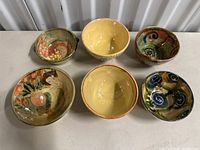 Lot overview showing all six ceramic bowls with varied colorful hand-painted designs placed on a white surface.