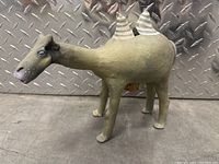 Front side view of a ceramic camel bank with two humps painted with white stripes, showing detailed facial features and textured surface.