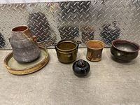 Lot of 5 ceramic items grouped together on concrete floor with metal diamond plate background.