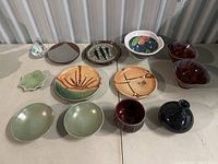 View of entire lot of 12 ceramic items on table, showing various plate and bowl shapes and colors