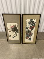 Two framed Chinese hand paintings leaning against wall