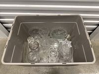 Top-down view inside plastic bin showing all crystal glassware items including vases, bowls, plates, and dishes in assorted clear glass with cut patterns.