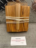 Front view showing wooden flower press with wedge inside wrapped string and instruction card.