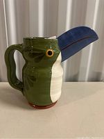Side view of the hand-painted bird shaped pitcher showing blue beak, green and white body and detailed eye