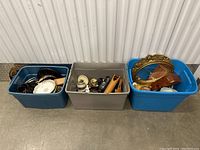 Three plastic bins filled with various porcelain and decorative items placed on a concrete floor.
