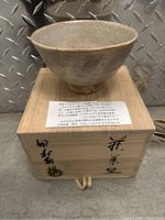 Front view of Japanese ceramic bowl on wooden box, showing bowl's glaze and texture, and wooden box top with Japanese calligraphy.