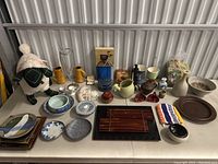 Full view of assorted ceramics, a plush sheep, bowls, plates, wooden art pieces, and other decorative objects arranged on a table inside a storage unit.