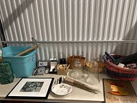 Wide view showing glass cloche jars, framed art, baskets, ceramic vase, and assorted small items on table.