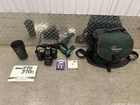 Full lot view showing Nikon F70 camera with attached lens, Tamron zoom lens with hood, Nikon F70 manual, two 52mm lens filters in cases, camera strap, and Lowepro camera bag.