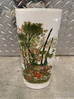 Front view showing cylindrical white porcelain vase with colorful peacock, floral and bamboo design and gold rim