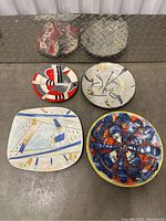 Four porcelain plates placed on floor, showing various artistic abstract designs and colors.