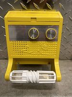 Front view of the yellow solid state radio with visible speaker holes, control knobs, and toilet paper holder.