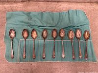 Ten sterling silver teaspoons on green cloth roll showing tarnish