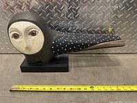 Side view of wood owl sculpture showing painted face, wing details, and measuring tape for size reference.