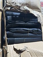 Box opened showing multiple black folded duffel bags stacked inside, secured with rubber bands