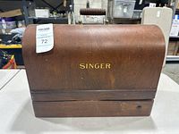Closed wooden carrying case for the Singer sewing machine with handle and gold 'SINGER' lettering.