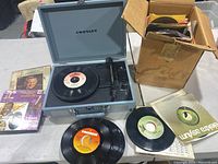 Blue Crosley portable record player open with 45 RPM vinyl record on turntable and control knobs visible.