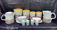 Full set including canisters with wooden lids, two pitchers, butter dish, four shakers, cup and saucer in green lattice and floral design