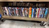 Wide view of a shelf with DVDs showing a variety of movie titles in plastic cases arranged side by side.