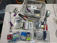 View of hardware and electrical tools including wire connectors, outlets, screws, wall anchors, faceplates, wire cutters, and strippers on a white surface with plastic baskets