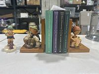 Two Hummel bookend figurines holding up 4 books by Joseph Ingolf Jacobsen on a flat surface