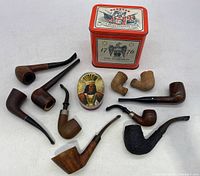 Group view of 10 tobacco pipes, 2 clay pipe end pieces, and 2 vintage tobacco tins with Bicentennial 1776-1976 theme and Native American chief illustration on tin lid.