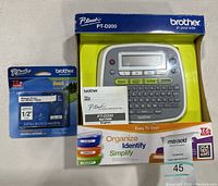 Brother P-Touch PT-D200 label maker in original box with user guide and MaxSold auction label, shown with the extra tape cartridge.