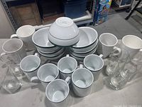 Variety of white ceramic bowls, white ceramic mugs, and clear glass mugs and glasses arranged on a table.