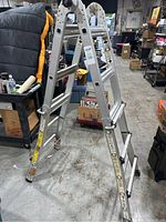 Full view showing the ladder folded into an A-frame shape with rubber feet on each leg, in a warehouse setting.