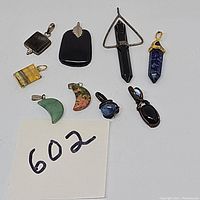 Top down view of all nine assorted stone pendants placed on white background, showing various shapes, colors and bails.