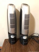 Front view of two silver and black ionic air purifier towers with vent slits and control dials on base.