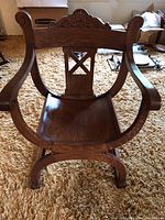Front angle view of antique wooden altar chair showing curved armrests, carved backrest with cross cutout, and solid seat.
