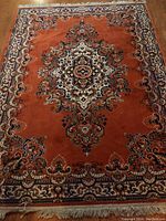 Full view of one area rug showing central floral medallion design and symmetrical border patterns on an orange pile.