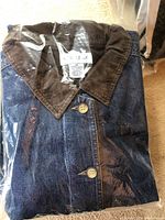 Photo of folded women's denim jacket in original plastic packaging highlighting button down front and collar.