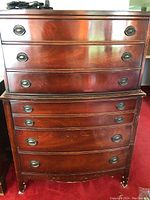 Front view of the two stacked sections of the reddish-brown wooden chest of drawers with three drawers each, showing oval metal ring pulls and some scratches.