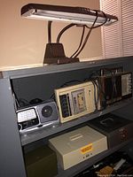 Photo showing vintage Atari 410 cassette tape recorder, portable radios, and desk lamp on a gray shelf.