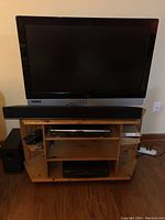 TV set up on wooden stand with sound bar in front and subwoofer nearby, showing general setup and included components.