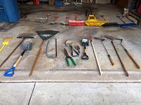 Full arrangement of the garden tools and snow shovels on a concrete floor showing the variety and condition.
