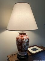 Close-up photo showing one ginger jar style lamp lit, featuring a red and white ceramic base with floral and geometric patterns, topped with a white fabric lampshade.
