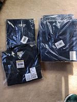 Two stacks of packaged L.L. Bean denim shirts and jumpers laid on carpeted floor.