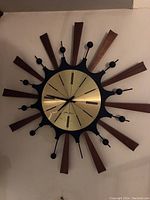 Full view of the sunburst clock mounted on wall showing wooden rays and black metal knobs, missing one knob at 5 o'clock.