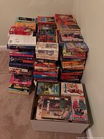 Stacks of multiple paperback books piled on the floor and in a box, showcasing the large quantity of the collection.