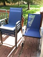 Four blue fabric patio chairs stacked and one chair set up individually on wooden deck.
