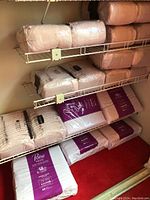 Packaged Poise adult pads and TENA adult diapers on wire shelves and floor in closet, close view of packaging and quantity.