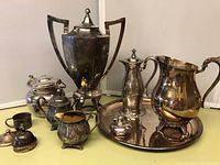 Group view of silverplated beverage set showing several items including pitcher, sugar bowl, creamer, and coffee urns.