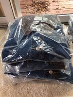 Stack of six blue denim women's jackets with brown collars, folded and in individual plastic packaging.