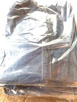 Photo of folded women's denim shirt inside clear plastic packaging, showing fabric and button detail