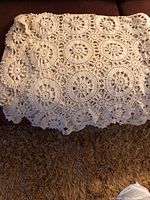 Photo showing part of the vintage crocheted tablecloth laid out, with visible circular floral lace motifs and scalloped edge detail.